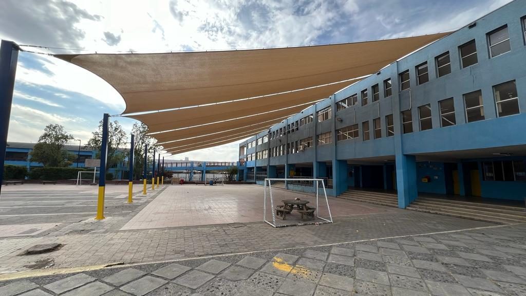 Grandes velas de sombra color arena sobre el patio de un establecimiento de fachada azul