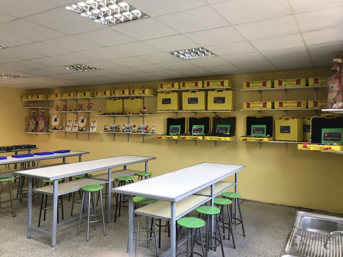 Sala de clases con mesones, piso y estantería equipada con material didáctico