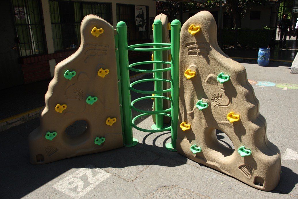 Mini muro de escalada infantil con presas de colores instalado en patio escolar
