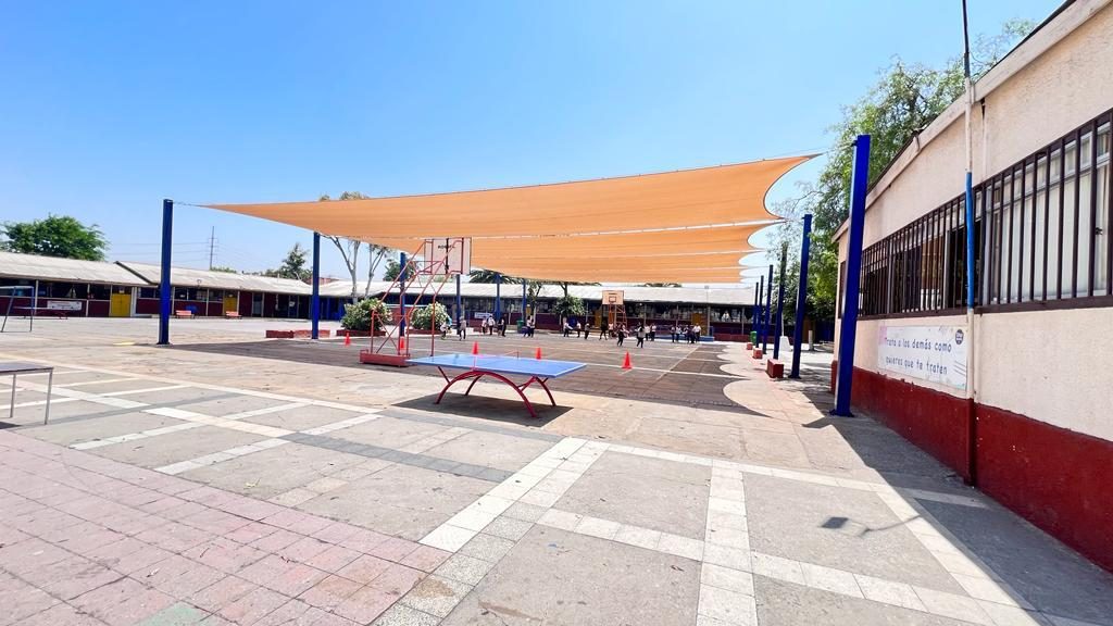 Velas de sombra cubriendo el patio interior de un colegio con graderías y aros de básquetbol